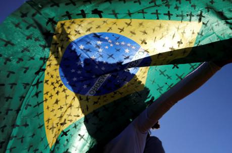 Un activista sostiene una bandera de Brasil, pintada con cruces que simbolizan a los muertos por la enfermedad del coronavirus, frente al Congreso Nacional, durante una protesta contra el presidente de Brasil, Jair Bolsonaro, en Brasilia. Foto: Archivo /