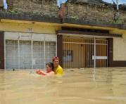 Un hombre ayuda a una mujer a cruzar una calle inundada por el río Piura